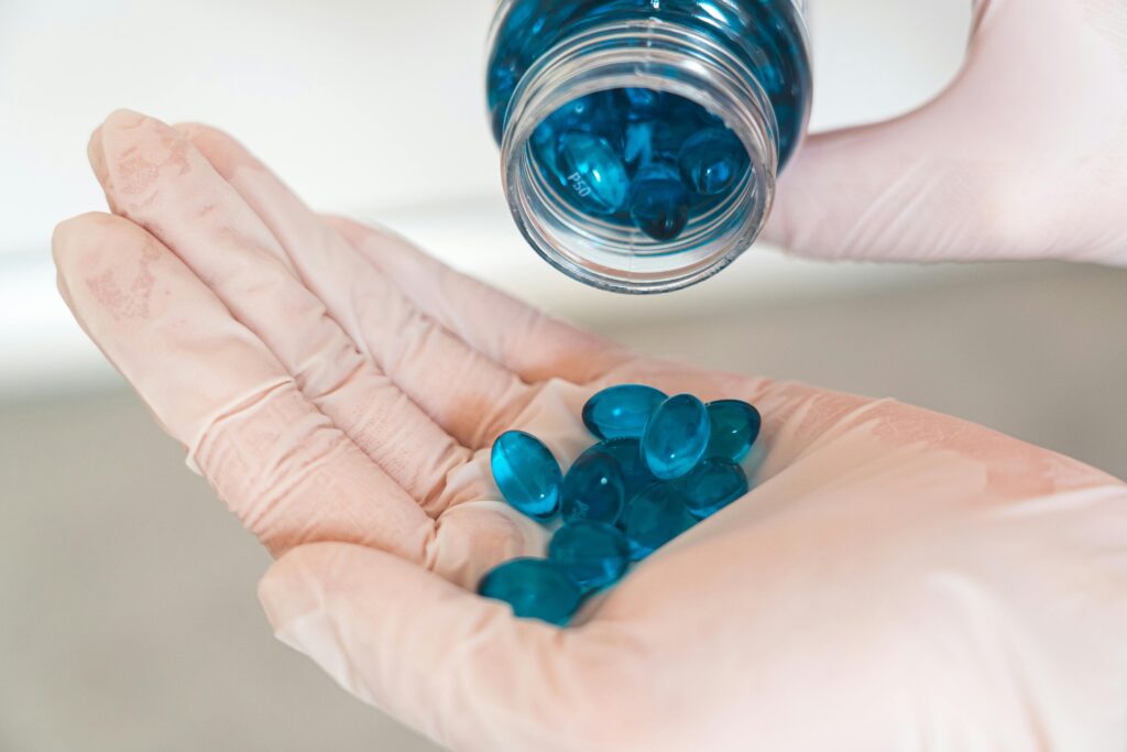 Close-up image of a healthcare worker with latex gloves pouring blue capsules from a bottle.