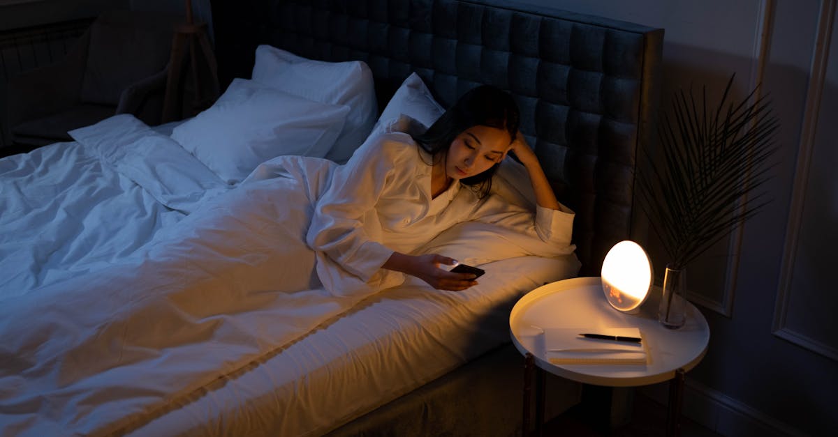 An Asian woman on a bed using her phone in a dim bedroom, reflecting on insomnia or night routines.
